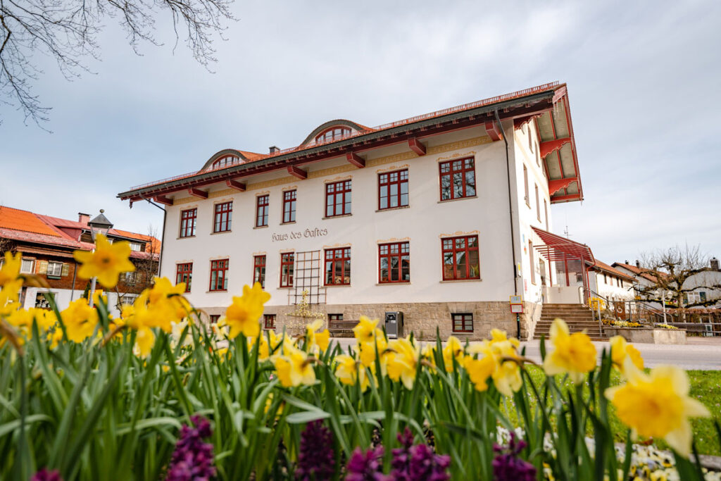 Blick auf das Rathausgebäude im Zentrum von Oberstaufen mit blühenden Sommerblumen im Vordergrund.