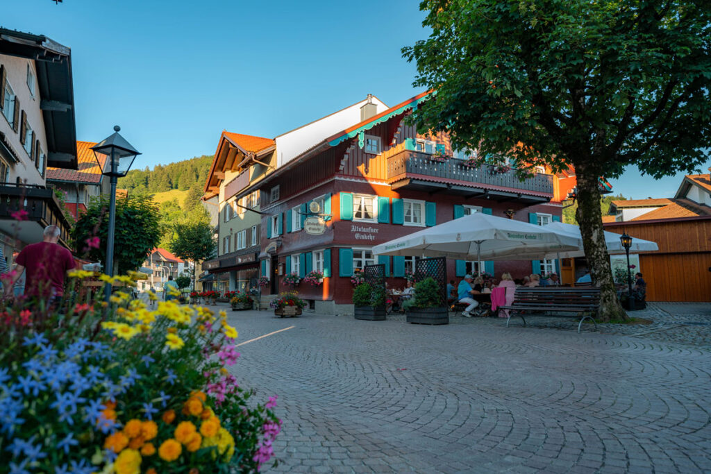 Gäste sitzen im Außenbereich eines Cafés an einer zentralen Straße in Oberstaufen.