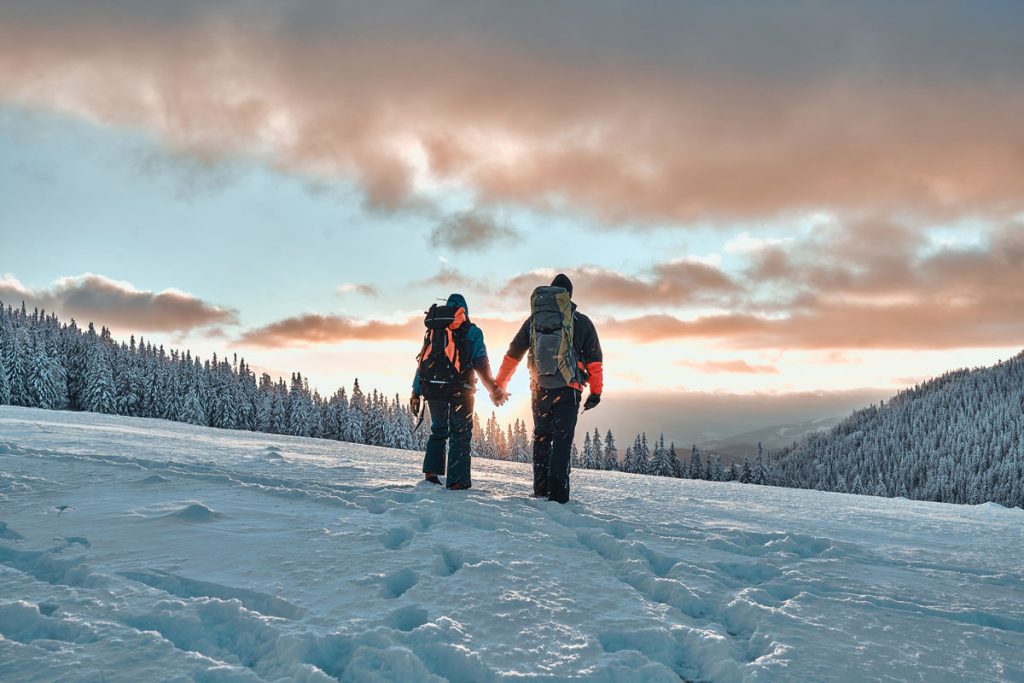Paar hält Händchen bei einem romantischen Winterspaziergang in Oberstaufen