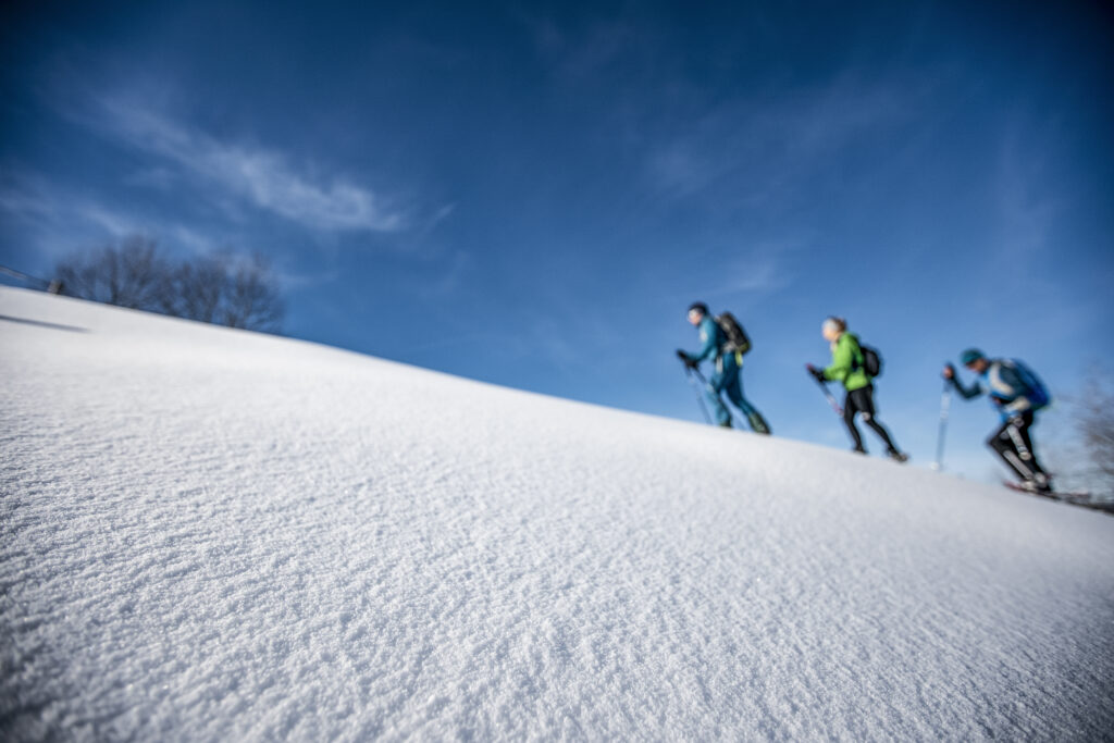 Menschen wandern mit Schneeschuhen durch den Tiefschnee in Oberstaufen