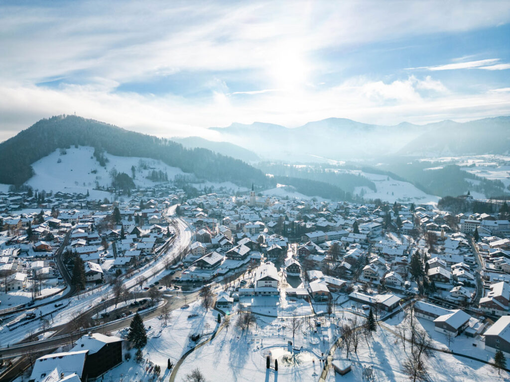 Blick über die schneebedeckten Dächer und den Kirchturm von Oberstaufen im Winter.