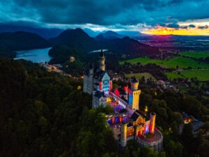 Vogelperspektive auf das illuminierte Schloss Neuschwanstein mit bunten Lichtern während eines Open-Air-Konzerts im Schlosshof