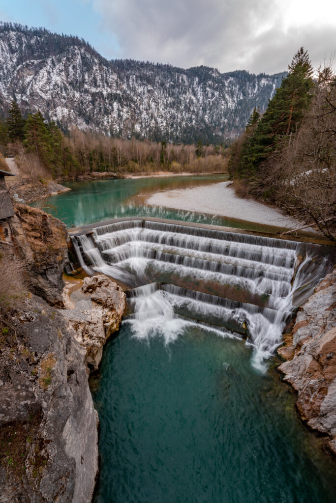 Der mehrstufige Lechfall bei Füssen stürzt in die enge Klamm mit Blick auf verschneite Allgäuer Berge.