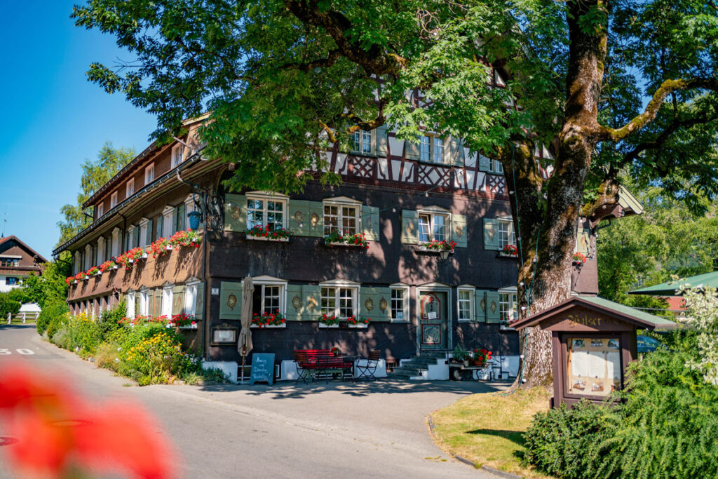 Ein traditionelles, schindelverkleidetes Allgäuer Bauernhaus mit üppigem Geranien-Blumenschmuck an den Fenstern in Thalkirchdorf.