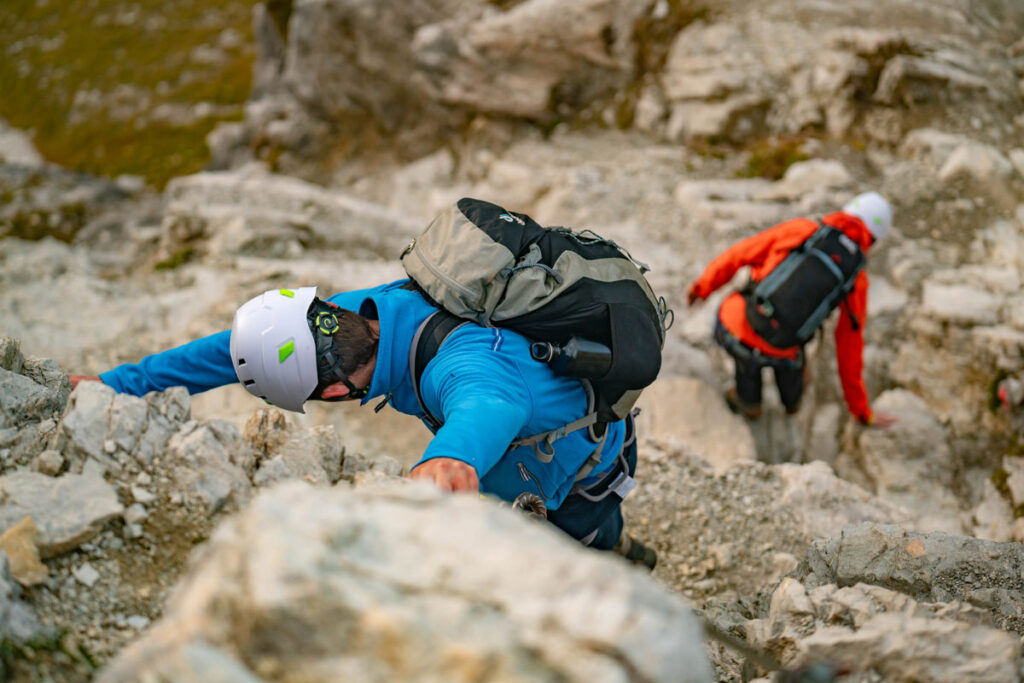 Zwei Bergsteiger im blauen und roten Outfit klettern eine steile Fels-Passage im Allgäu hinauf.
