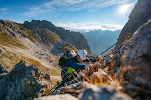 Ein gut gesicherter Kletterer steigt am Drahtseil des Mindelheimer Klettersteigs im Allgäu steil nach oben.
