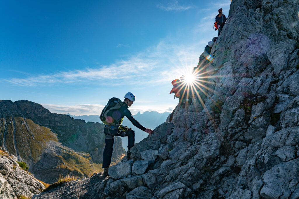 Ein Bergsteiger geht bei strahlendem Sonnenschein über einen exponierten Felsgrat im Allgäu.