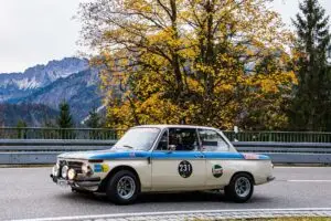 Historischer BMW 2002 Rennwagen bei der Gleichmäßigkeitsprüfung auf der Jochpass-Strecke vor herbstlichem Bergpanorama.